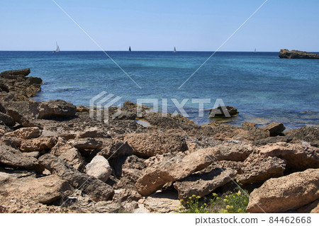 Rocky beach and calm water with sailing boats Rocky beach and calm water with sailing boats 84462668