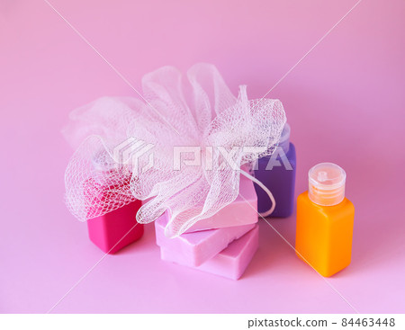 Colorful washcloth, plastic travel bottles and bars of soap on a soft pink background. Accessories for body care and hygiene. 84463448