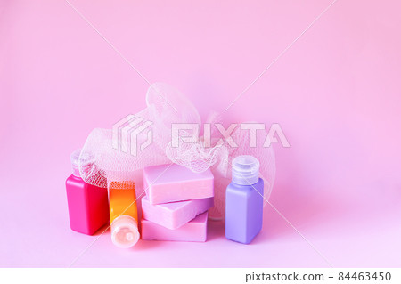 Colorful washcloth, plastic travel bottles and bars of soap on a soft pink background. Accessories for body care and hygiene. 84463450