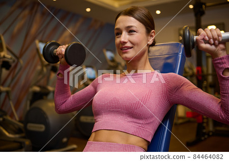 Middle aged muscular beautiful athletic woman doing exercise for arms, working out with dumbbells at gym. Strength and motivation concept. Healthy lifestyle, sport, fitness 84464082