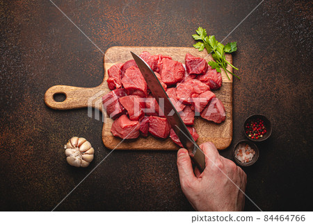 Male hand chopping in cubes raw beef meat on wooden board Male hand chopping in cubes raw beef meat on wooden board 84464766
