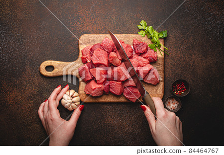 Female hands chopping in cubes raw beef meat on wooden board 84464767