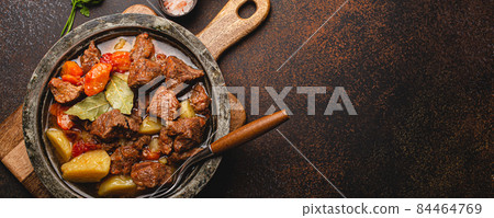 Meat beef stew with vegetables and gravy in rustic metal pot top view copy space Meat beef stew with vegetables and gravy in rustic metal pot top view copy space 84464769