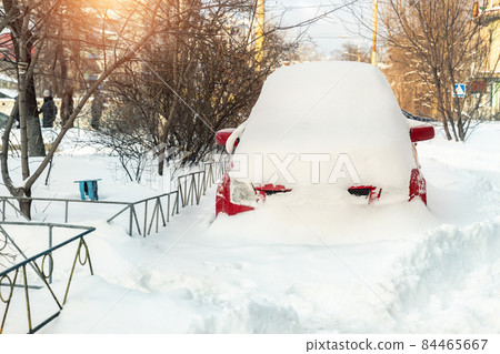 City street driveway parking lot spot with small car covered snow stuck trapped after heavy blizzard snowfall winter day by big snowy pile. Snowdrifts and freezed vehicles. Extreme weather conditions City street driveway parking lot spot with small car covered snow stuck trapped after heavy blizzard snowfall winter day by big snowy pile. Snowdrifts and freezed vehicles. Extreme weather conditions 84465667