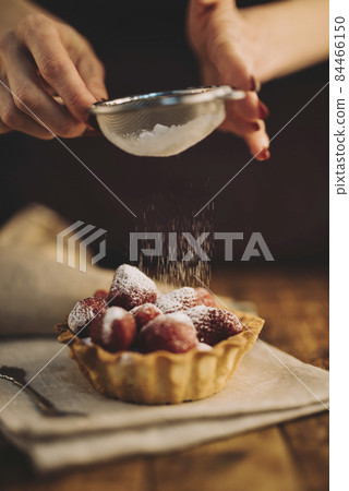 woman dusting sugar powder strawberry tart. High quality photo woman dusting sugar powder strawberry tart. High quality photo 84466150
