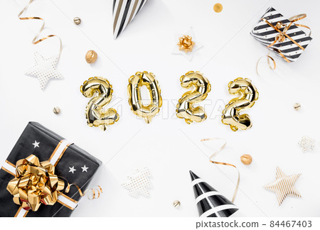 Happy New year 2022 celebration card. Gold foil balloons numeral 2022 on white background. Gifts and party hats. Happy New year 2022 celebration card. Gold foil balloons numeral 2022 on white background. Gifts and party hats. 84467403