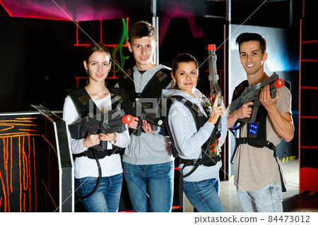 Four happy young men an women posing with laser pistols in their hands in dark laser tag room 84473012