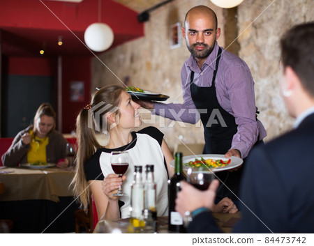 Friendly guy waiter serving meals to young couple 84473742