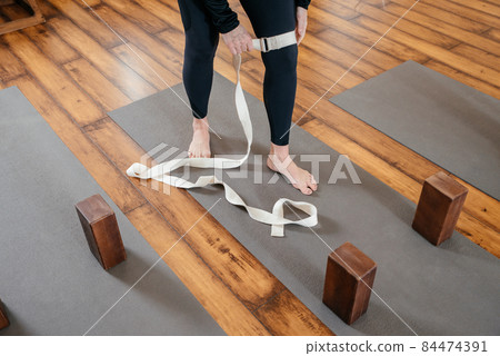 Cropped view of woman stretching her leg with strap in yoga studio Cropped view of woman stretching her leg with strap in yoga studio 84474391