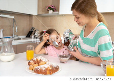 Mother having breakfast with her daughter at a table in kitchen, happy single mother concept 84474765
