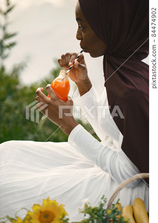 Portrait of a muslim woman sitting near the river and drinking an orange juice Portrait of a muslim woman sitting near the river and drinking an orange juice 84474902