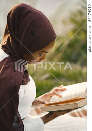 Portrait of a muslim woman sits on the plaid picnic blanket near the river 84474910