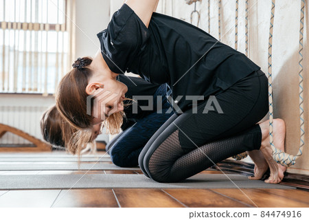 Lyengar female group of yogi practicing calisthenics exercise in yoga studio hanging on a wall with ropes 84474916