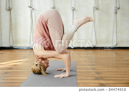 Mature woman doing headstand yoga pose in studio Mature woman doing headstand yoga pose in studio 84474918