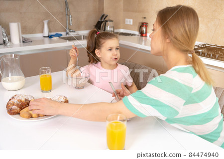 Mother having breakfast with her daughter at a table in kitchen, happy single mother concept 84474940