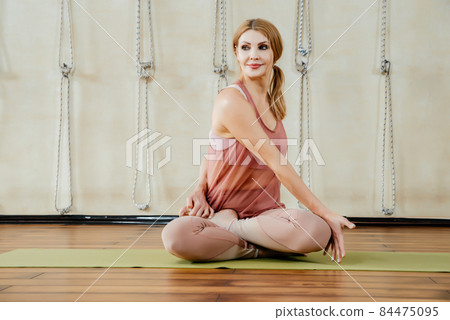 Mature woman practicing yoga sitting in twisting pose on a floor Mature woman practicing yoga sitting in twisting pose on a floor 84475095