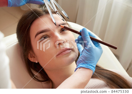 Cosmetologist measures the proportions of the eyebrows with the ruler. 84475330