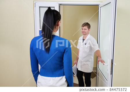 Doctor welcoming a woman patient to his office opening door in modern clinic 84475372