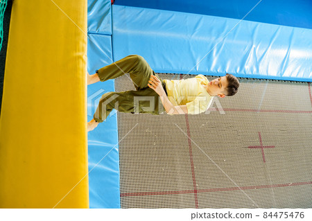 Teenage boy jumping on trampoline park in sport center Teenage boy jumping on trampoline park in sport center 84475476