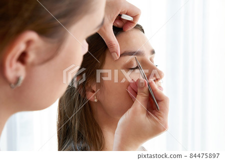 Plucking female eyebrows with tweezers during eyebrow correction in beauty salon Plucking female eyebrows with tweezers during eyebrow correction in beauty salon 84475897