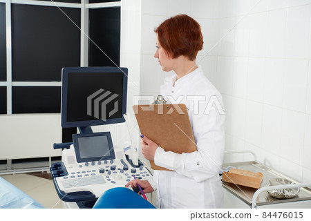 Professional doctor with clipboard near modern ultrasound machine in clinic 84476015