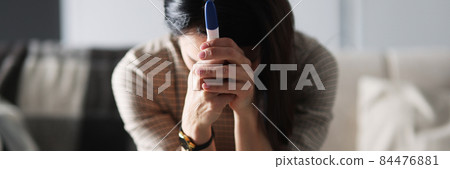 Upset woman is sitting on couch and holding pregnancy test 84476881