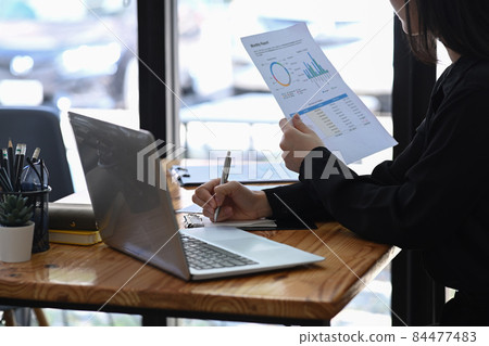 Businesswoman sitting in front of laptop computer and analyzing financial document. Businesswoman sitting in front of laptop computer and analyzing financial document. 84477483