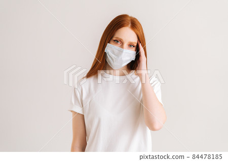 Studio portrait of attractive young woman wearing casual t-shirt and protective face mask looking at camera standing on white isolated background. Studio portrait of attractive young woman wearing casual t-shirt and protective face mask looking at camera standing on white isolated background. 84478185