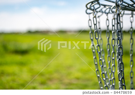 Disc golf goal chains gently swaying in the breeze with a green course in the background Disc golf goal chains gently swaying in the breeze with a green course in the background 84478659
