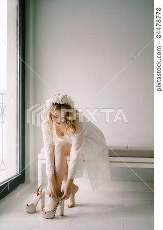 Bride in white lace peignoir wears high-heeled sandals in preparation for the wedding ceremony Bride in white lace peignoir wears high-heeled sandals in preparation for the wedding ceremony 84478778