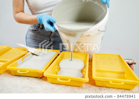 Young woman pouring paint into plastic paint tray Young woman pouring paint into plastic paint tray 84478941