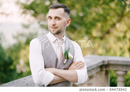 Groom crossed his arms over his chest near the balustrade in the garden. Portrait Groom crossed his arms over his chest near the balustrade in the garden. Portrait 84478942