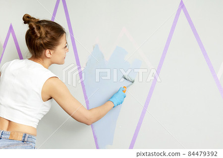 Back view of girl painting wall with paint roller and using masking tape while standing on ladder Back view of girl painting wall with paint roller and using masking tape while standing on ladder 84479392
