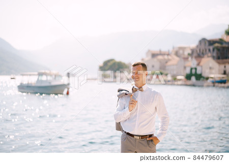 Groom with a jacket on his shoulder against the background of buildings and a ship Groom with a jacket on his shoulder against the background of buildings and a ship 84479607
