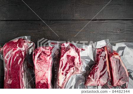Vacuum packed organic raw beef classic cuts, tomahawk, t bone, club steak, rib eye and tenderloin cuts, on black wooden table background, top view flat lay, with copy space for text Vacuum packed organic raw beef classic cuts, tomahawk, t bone, club steak, rib eye and tenderloin cuts, on black wooden table background, top view flat lay, with copy space for text 84482344