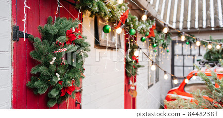a red car by the porch of the house with a new year's wreath on the red door.  84482381
