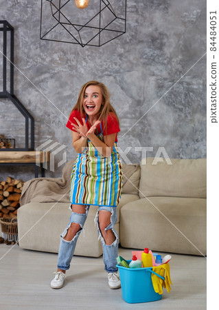 Happy young cleaning woman in apron with mop rejoicing in living room. Perfect order 84484051