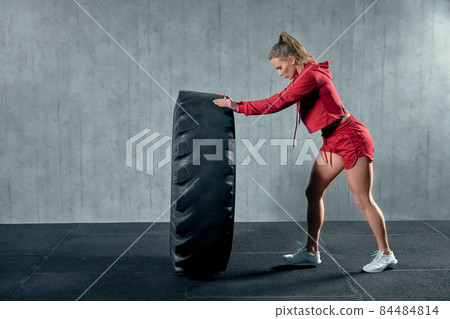 Fit female athlete working out with a huge tire, turning and flipping in the gym. Fit female athlete working out with a huge tire, turning and flipping in the gym. 84484814