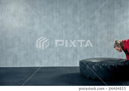 Fit female athlete working out with a huge tire, turning and flipping in the gym. 84484815