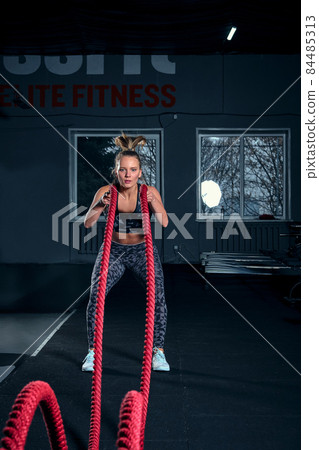 Vertical full length shot of an athletic fitness woman doing functional training exercise with battle ropes at the gym CrossFit cross training strength endurance energy power concept 84485313