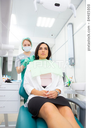 The dentist's assistant puts a protection on the patient, a napkin on the chest. Preparing for dental treatment 84485808