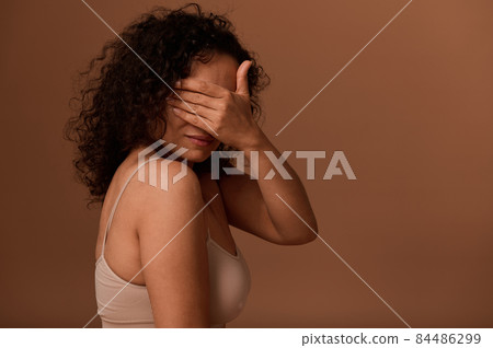 Dark-haired woman in underwear hides her face, covering it with her hand. Concept of body positivity, self-confidence, end violence and oppression against women 84486299