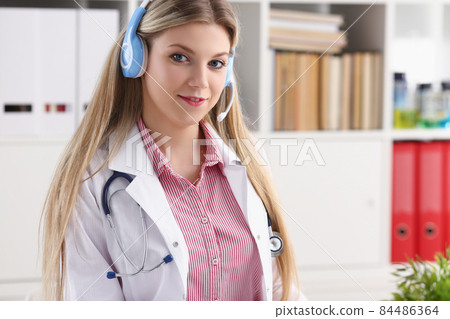 Pretty female blonde doctor talking to patient over wireless headset advises medical problem Pretty female blonde doctor talking to patient over wireless headset advises medical problem 84486364