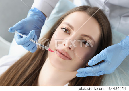 Young woman gets injection of botox in her lips, cosmetologist using syringe Young woman gets injection of botox in her lips, cosmetologist using syringe 84486454