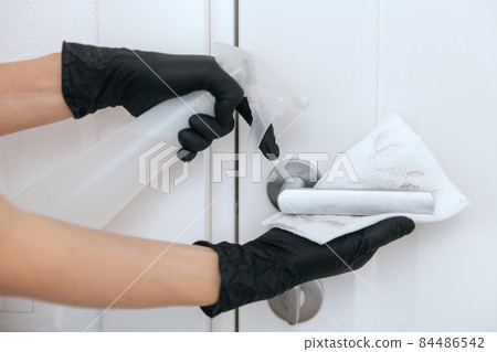Cleaning door handle with dirty wipe in black gloves and sanitizer spray. Disinfection in hospital and public spaces against corona virus. Woman hand using towel for cleaning. 84486542
