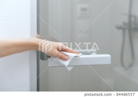 Cleaning glass door handles with an antiseptic wet wipe. Sanitize surfaces prevention in hospital and public spaces against corona virus. Woman hand using towel for cleaning home room door link. Cleaning glass door handles with an antiseptic wet wipe. Sanitize surfaces prevention in hospital and public spaces against corona virus. Woman hand using towel for cleaning home room door link. 84486557