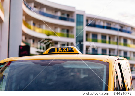 a taxi sign on the roof of a yellow car. 84486775