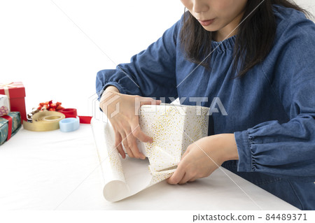 A woman's hand wrapping a gift in wrapping paper at the living room table 84489371