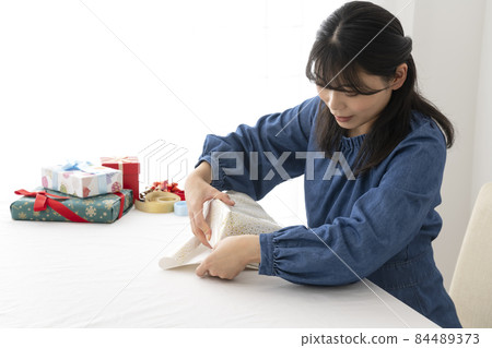 一個女人在客廳的桌子上用包裝紙包裝禮物 84489373
