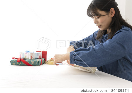 一個女人在客廳的桌子上用包裝紙包裝禮物 84489374